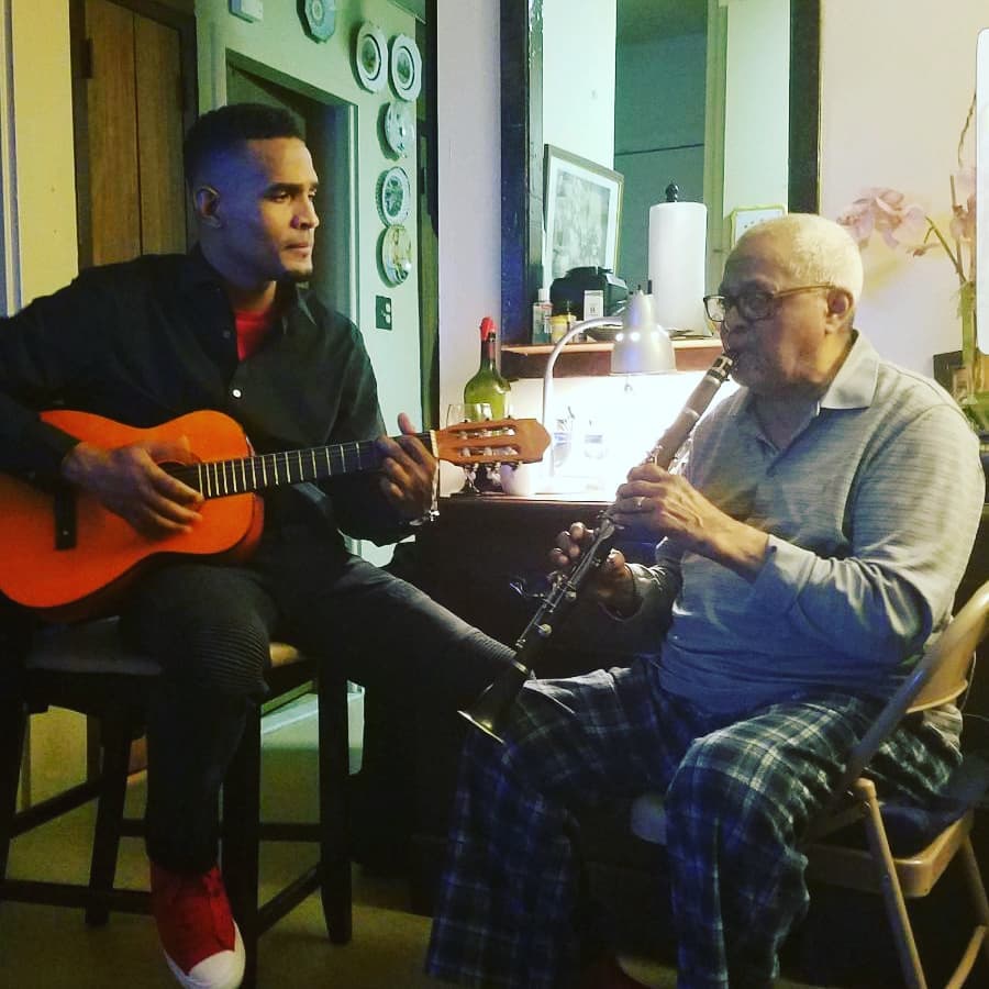 Charlie Pe tocando guitarra junto a un clarinetista mayor en casa (2018)