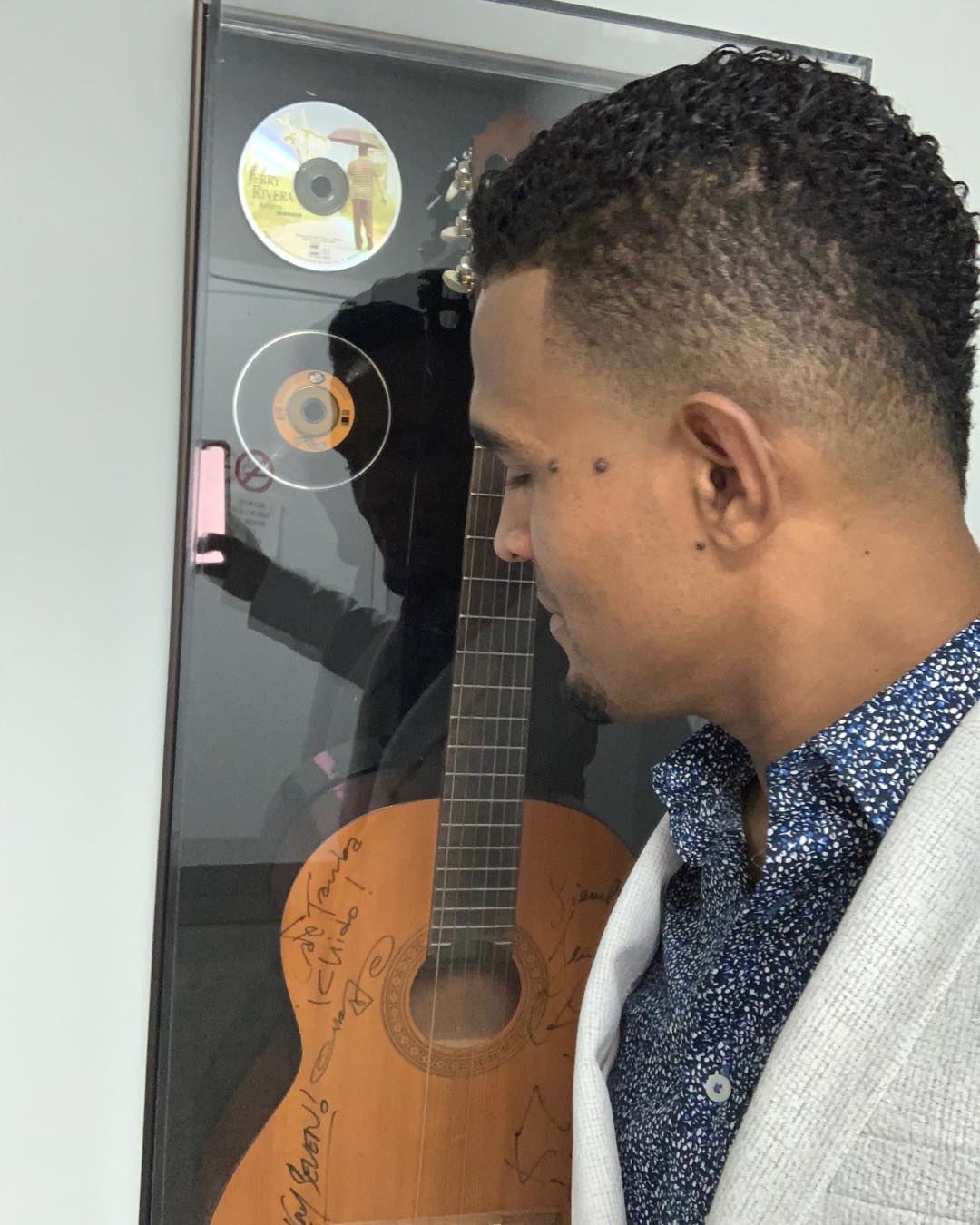 Charlie Pe con una guitarra frente a discos de oro enmarcados en la pared (2019)
